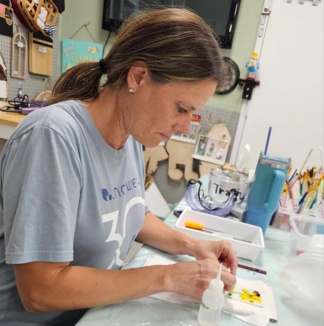 A workshop participant carefully arranges small glass pieces on a project tile at Glass Quiltopia.