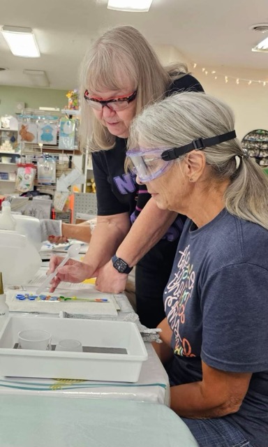 Joanne Fransen-Gilliam assists a workshop participant wearing safety glasses with a fused glass project.