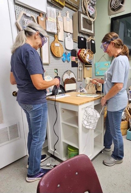 Two workshop participants work with glass tools and supplies at a Glass Quiltopia studio station.