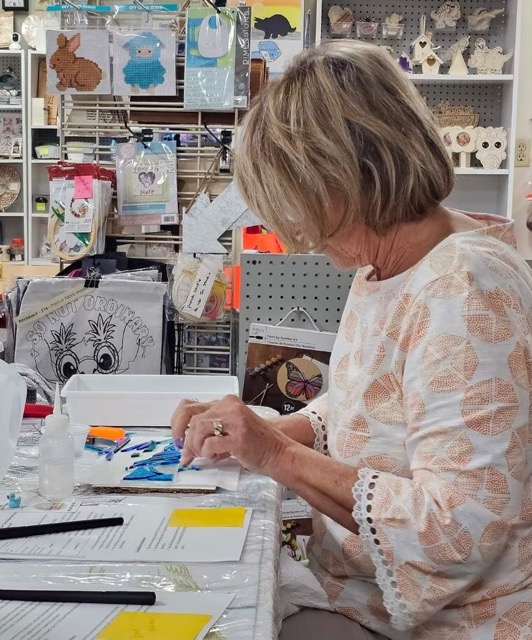 A workshop participant places blue glass pieces on a project during a Glass Quiltopia class.